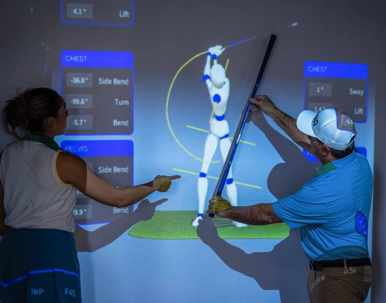 Coach demonstrating 3D swing analysis with Sportsbox AI, showing a golfer’s body mechanics and movement data projected on a screen at Studio Golf.